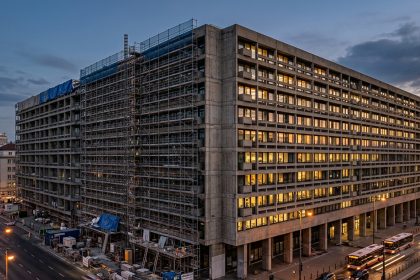Edificio de oficinas en proceso de renovación, con andamios en una de sus fachadas mientras el resto de la estructura permanece operativo e iluminado