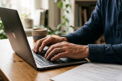 Primer plano de las manos de un hombre elaborando un currículum vitae competitivo en una computadora portátil desde su hogar.