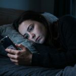 mujer en penumbras en la cama mirando el teléfono, representando la dificultad para la desconexión laboral