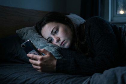mujer en penumbras en la cama mirando el teléfono, representando la dificultad para la desconexión laboral